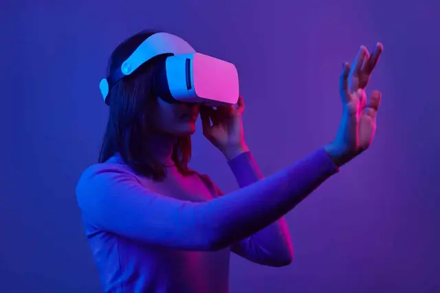 Mujer joven con un visor blanco de realidad virtual y una mano extendida, bajo una luz violeta y rosada que sugiere un entorno digital