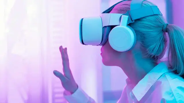 Mujer con visor de realidad virtual y auriculares que levanta una mano, en un ambiente de luz rosada y violeta