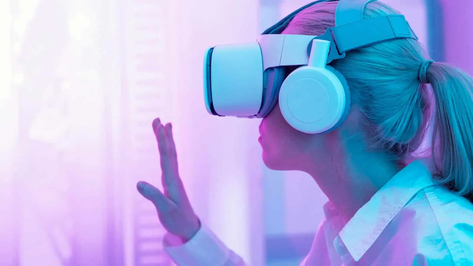 Mujer con visor de realidad virtual y auriculares que levanta una mano, en un ambiente de luz rosada y violeta