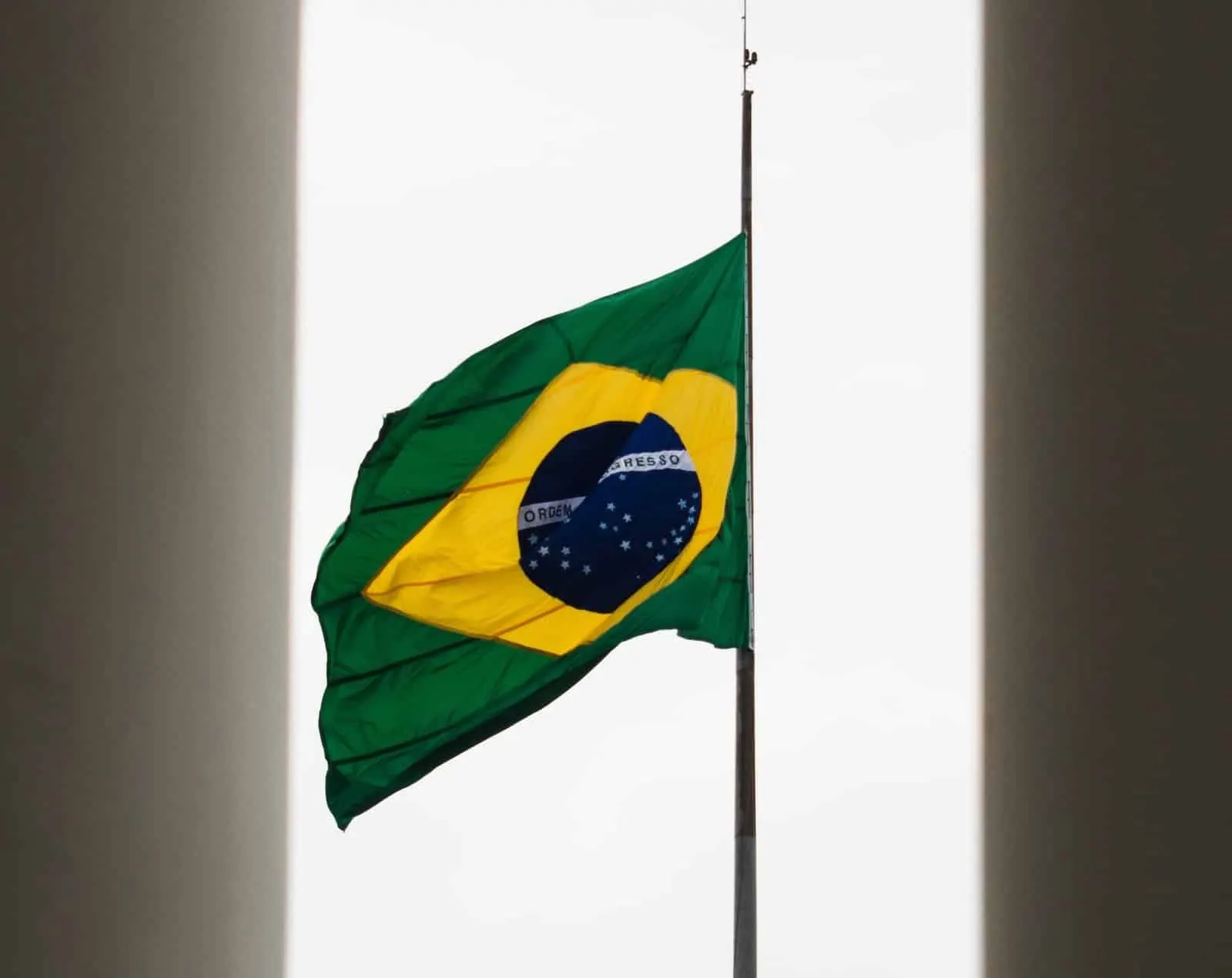 Bandera de Brasil izada a media asta contra un cielo blanco, entre dos muros oscuros