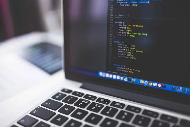 Portátil con código de programación en pantalla y un teclado en primer plano, con el fondo desenfocado