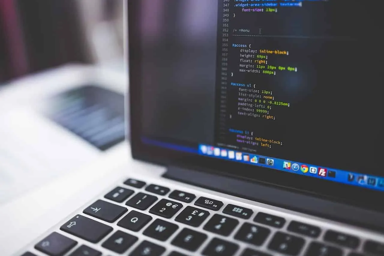 Portátil con código de programación en pantalla y un teclado en primer plano, con el fondo desenfocado