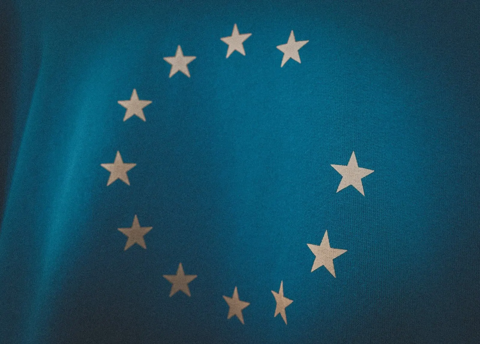 Bandera de la Unión Europea, con su círculo de estrellas blancas sobre fondo azul, en una toma cercana y oscura