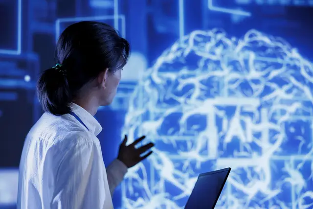 Mujer de perfil que levanta una mano ante un gran cerebro luminoso en azul, con una laptop en primer plano y la sigla AI en la imagen.