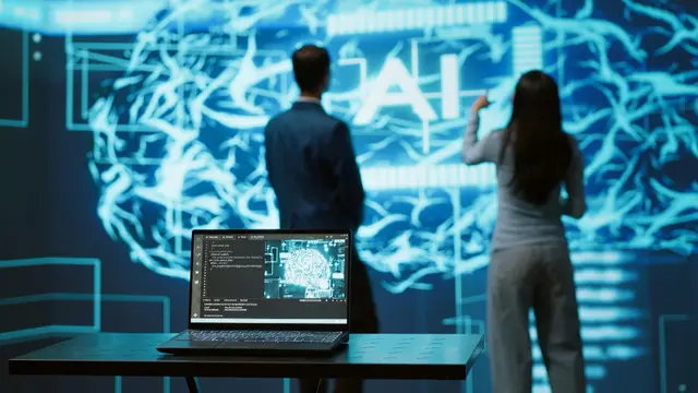 Un hombre de traje y una mujer de espaldas frente a un gran cerebro luminoso con las letras AI, con una laptop en primer plano.