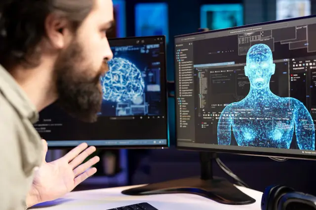 Hombre de perfil con la mano en el mentón frente a un monitor que muestra un cerebro luminoso, en una sala con luz cálida.