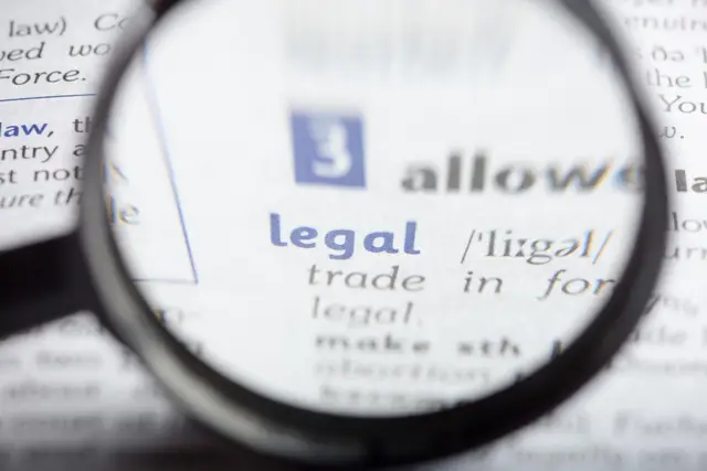 Lupa que amplía la palabra «legal» en una entrada de diccionario, con letras azules y grises desenfocadas alrededor.