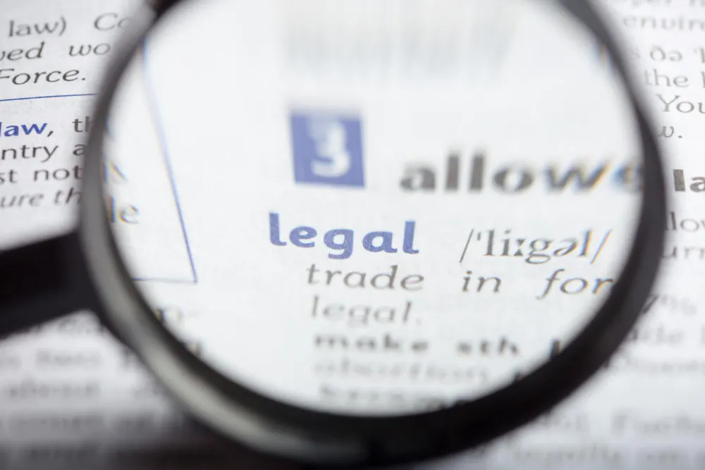 Lupa que amplía la palabra «legal» en una entrada de diccionario, con letras azules y grises desenfocadas alrededor.