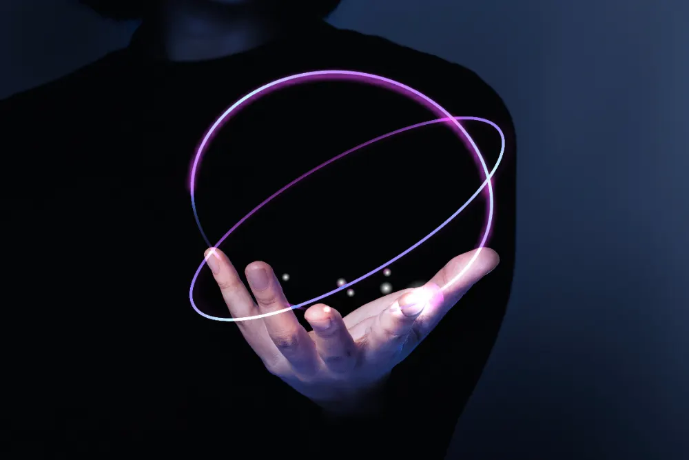 Una mano abierta de una persona vestida de negro sostiene un doble anillo luminoso violeta que forma una esfera.