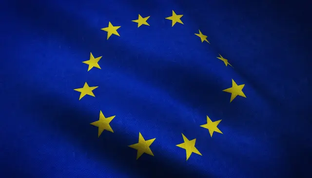 Bandera de la Unión Europea ondeando, con doce estrellas amarillas en círculo sobre fondo azul.