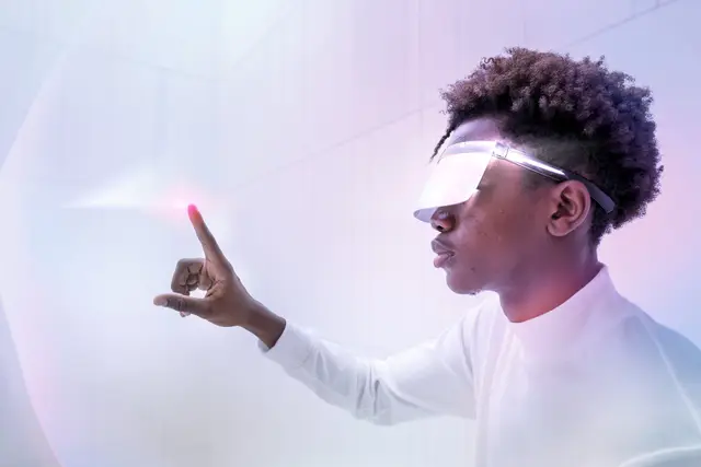 Joven con visor transparente que señala con el dedo un punto de luz rosada sobre un fondo blanco y violeta.