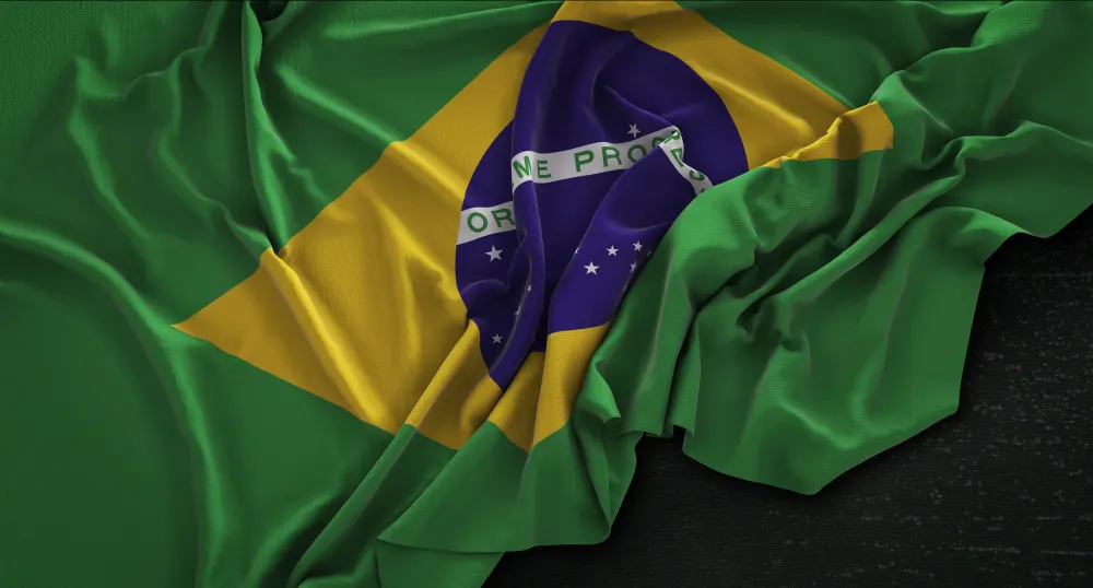 Bandera de Brasil arrugada, con el rombo amarillo y el círculo azul con estrellas, sobre un fondo oscuro.
