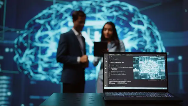 Un hombre y una mujer de pie, desenfocados, frente a la proyección luminosa de un cerebro, con una laptop con código en primer plano
