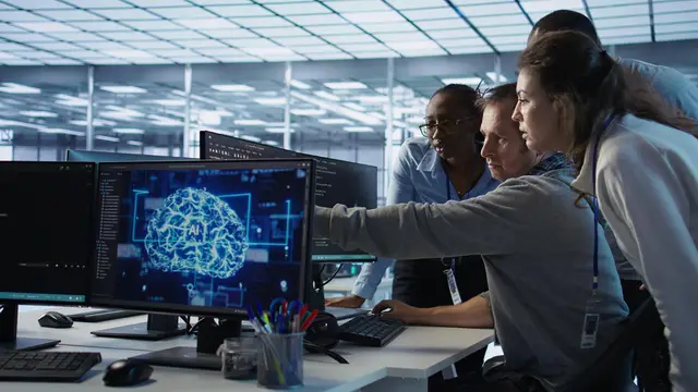 Un equipo de profesionales observa un monitor que muestra un cerebro digital con las letras AI en una oficina luminosa