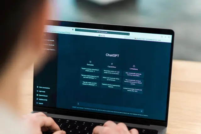 Persona que escribe en una laptop con la pantalla de inicio de ChatGPT, que muestra ejemplos, capacidades y limitaciones del chatbot