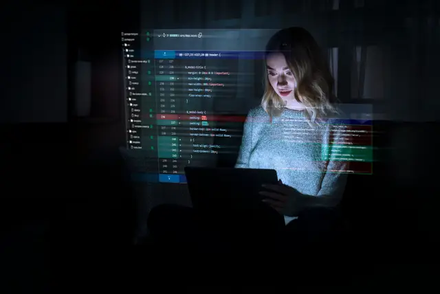 Mujer frente a una laptop en una habitación oscura, con líneas de código proyectadas sobre ella, imagen del desarrollo de software de inteligencia artificial