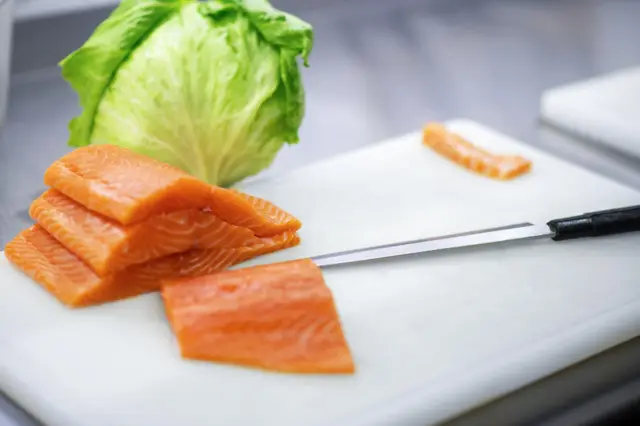 Filetes de salmón crudo sobre una tabla blanca junto a una hoja de lechuga