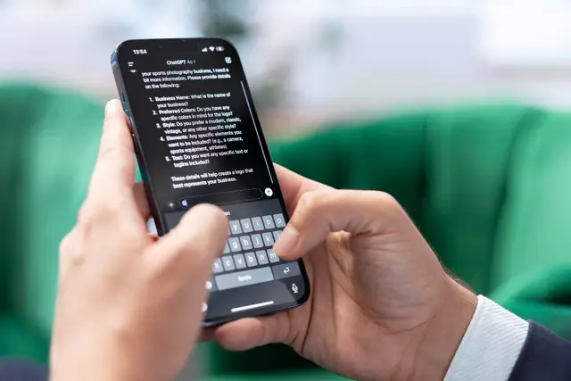 Manos sostienen un teléfono móvil con una conversación de ChatGPT en pantalla, frente a un sofá verde