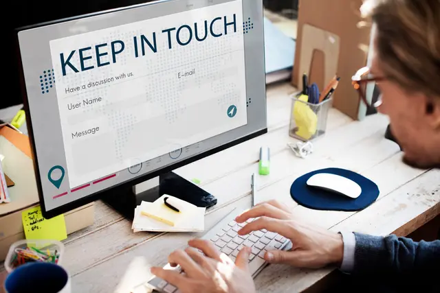 Hombre con gafas que escribe en un teclado frente a un monitor con un formulario de contacto titulado «Keep in touch»